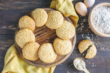 Sesame biscuits, homemade healthy snack. Honey bars with sesame seeds on old wooden board with ingredients for cooking -  eggs, flour on rustic table. Top view, flat lay, copy space.