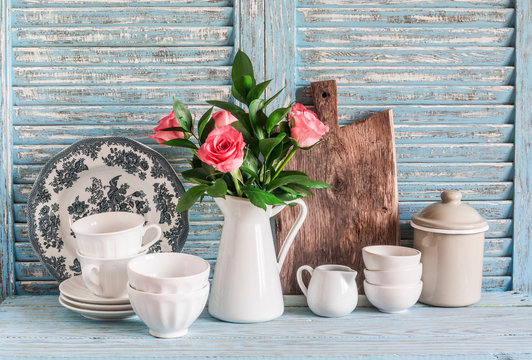 Roses In A White Pitcher, Vintage Crockery On Blue Wooden Rustic Background. Kitchen Still Life In Vintage Country Style. Flat Lay