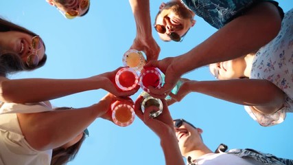 Low angle view of friends having fun at pool party, clinking glasses with colorful summer cocktails near hotel swimming pool. People toast drinking fresh juice at luxury summer villa in slow motion. - Powered by Adobe