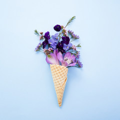 Purple flowers in waffles in flat style on blue background. Flatlay, top view. Birthday, spring background.