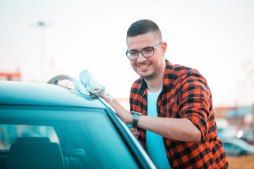 Happy young man carefully cleaning his car with microfiber cloth