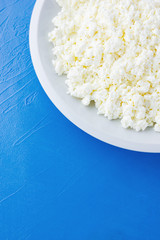 Cottage cheese in a white plate on a blue background. Organic eco healthy meal, dairy product. Plate of homemade cottage cheese. Top view. Copy space