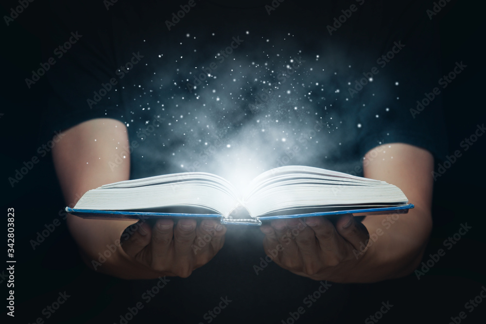 Wall mural man open magic book with growing lights and magic powder floating on the book, learning, education, 