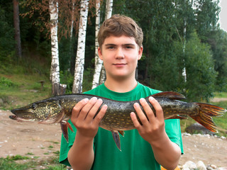 Summer. Karelia. The shore of Lake Ladoga. A young man holds a pike in his hands. In the background...