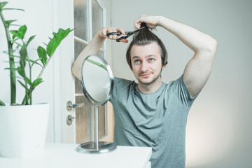 Caucasian shaggy man trying to make a haircut by himself with scissors being on quarantine during...