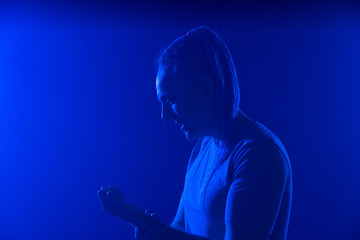 Portrait of a man in with an unusual haircut mohawk iboxing in blue darkness background