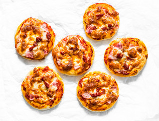 Mini ham, tomato sauce, mozzarella pizza on a light background, top view. Delicious breakfast, snack, tapas