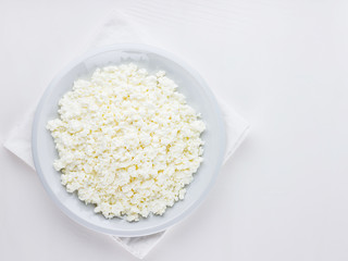 Cottage cheese in a plate on a white background. Cottage cheese on a white napkin. Top view. Copy space