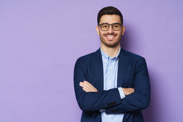 Young buisnessman wearing eyeglasses, jacket and shirt, holding arms crossed, looking at camera...