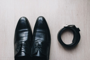 Black men's shoes for a businessman and a leather belt stand on the background of parquet. Photography, concept. Morning and preparation of the groom.