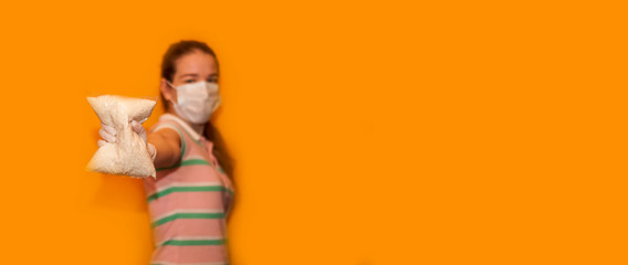 a young girl in gloves on an orange background with a packet of rice in her hands. product delivery concept. Funny and with tails, Copyspace for text, banner