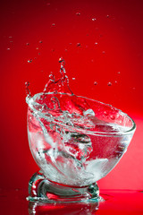 A splash of a drink in a glass, shot against a bright red background.