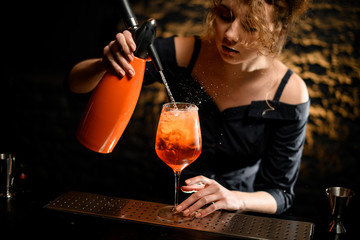 woman bartender carefully pour liquid from orange siphon to glass with bright drink