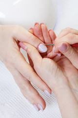Woman in nail salon receiving manicure by beautician. Close up shot of a beautician applying nail polish to female nail in a nail salon.