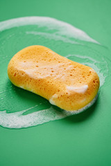 Yellow washing sponge in soap foam on a green background close up isolated