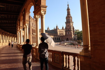 Two man walking with black umbrella for sun on the porch in Plaza de Espana in Seville