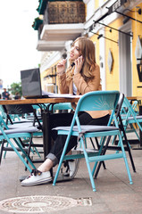 Beautiful young woman working with a laptop in a city cafe and talking on the phone.	