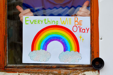 Image of a rainbow on a white sheet of paper behind glass in an old window. Hands hold a drawing. A...