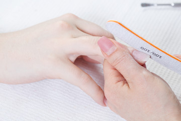 Manicure process in beauty salon, close up. Manicurist filing client's nails at table, closeup. Woman in nail salon receiving manicure by beautician.