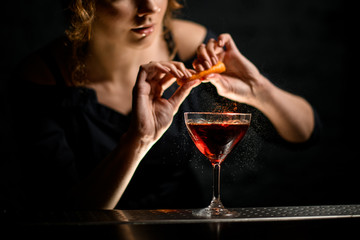 Woman barman neatly sprinkles citrus juice on glass with drink.