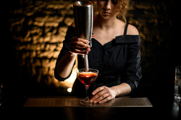 Woman bartender holds foam blower over glass with cocktail.