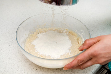 Woman's hands with an yeast dough. The woman is adding flour to the glass bowl with dough..