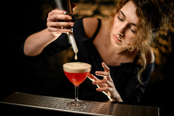 Woman bartender add foam to glass with cocktail and looks at it