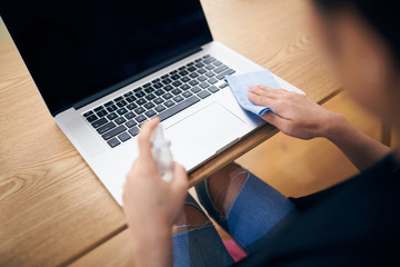 Woman wiping and sterilizing her laptop with alcohol spray and antistatic cloth at home office.