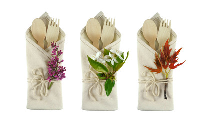 Natural cutlery collection: wooden spoon and fork in linen napkin decorated with lilac, cherry flowers and young maple sprig. Set isolated on white background. Spring country style table setting.