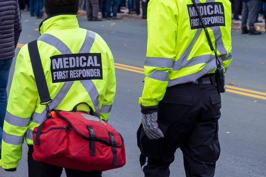 Two medical responders walking in a street with bright yellow coats with the words medical first responder on a black background with grey lettering. One medical officer is carrying a first aid bag.