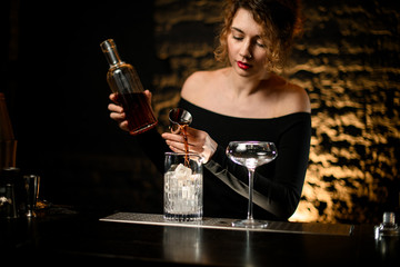 sexy woman bartender gently pours alcoholic drink from jigger into glass with ice