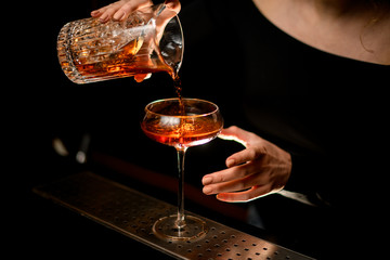 Close-up. Bartender girl in dark room gently pours drink into glass