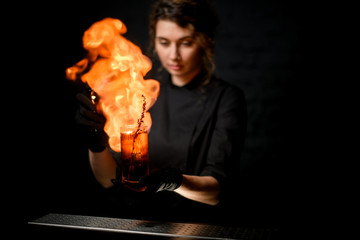 woman bartender neatly decorates cocktail glass with flowering branch, spray on it and sets on fire.