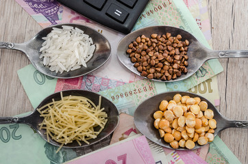 composition with various types of legumes and cereals in spoons on a wooden table. Organic grains and dollars. The concept of economic crisis and rising prices. Rice, buckwheat, pasta and hryvnia.