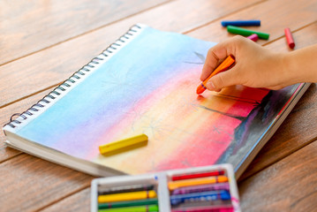 A girl painting a colorful landscape with wax crayon on a drawing pad