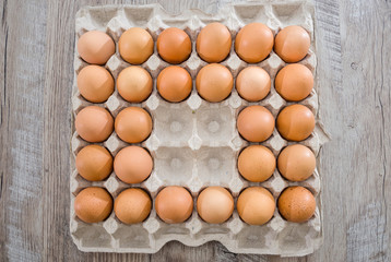 Chicken eggs in a cardboard box on a wooden table without four eggs.