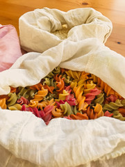 Organic colorful pasta in reusable bag close up. Groceries in reusable textile bags on wooden table. Plastic free delivery from bulk store. Zero waste shopping. Ban plastic