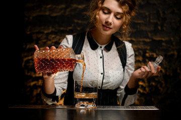 woman bartender accurate pours alcoholic drink from decanter into glass.