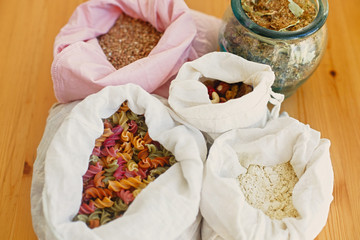 Groceries in reusable textile bags on wooden table. Cereals,pasta, flour, grains in bags, tea in glass jar. Plastic free delivery from bulk store. Zero waste shopping. Ban plastic