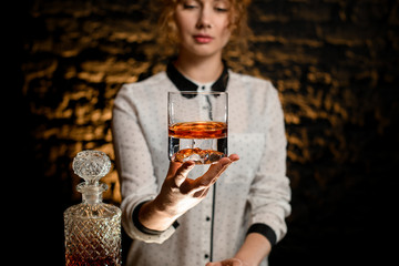 Young beautiful bartender woman hold old-fashioned glass with alcoholic drink