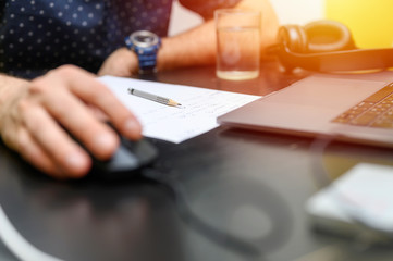 work from home. workplace with a laptop, glass of water and paper for notes. working man. male hands using a computer mouse. selective focus. flare