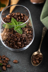 Coffee beans in glas with mint leaves on green background