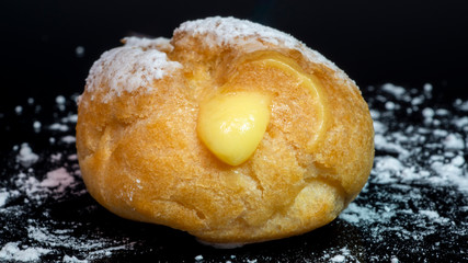 Delicious cream puff filled with custard. Italian bignè. Close-up on a black background