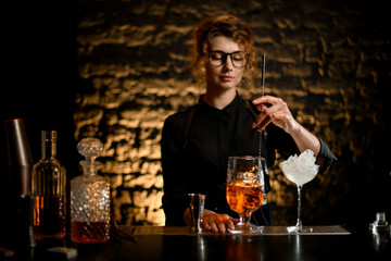 Woman bartender mix cold cocktail with spoon in glassy mixing cup.