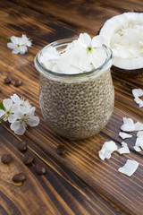 Coffee pudding with chia and coconut flakes  in the glass jar on the brown wooden background.  Location vertical.