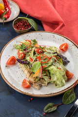 Fresh salad with chicken breast, lettuce and tomatoeson white plate on blue red background