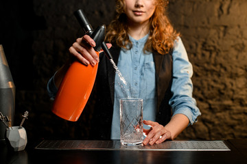 bartender girl holds orange siphon and pours water from it