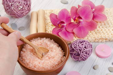 SPA body care concept. Bath salt, washcloth, candle and pink Orchid flower on white wooden background