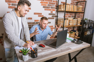 two young men, business people working remotely in the office, sitting at a desk, working with documents, discussing work, emotionally, thinking, tired after work and from work