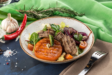 Warm salad with grilled veal, tomato, onion and lettuce on blue green background